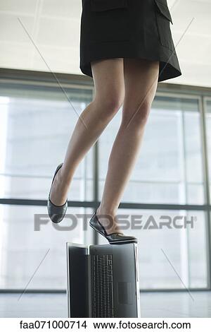 Picture - Woman standing on top of laptop computer, low section. Fotosearch
