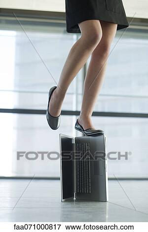 Stock Photo - Woman standing on top of laptop computer, low section. Fotosearch