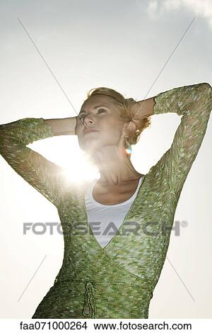 Woman with hands behind head contemplating outdoors View Large Photo Image Picture - Woman with hands behind head contemplating outdoors. Fotosearch