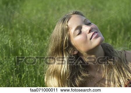 Stock Image - Young woman relaxing in field of grass. Fotosearch