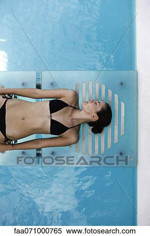 Stock Photography - Young woman sunbathing by pool. Fotosearch