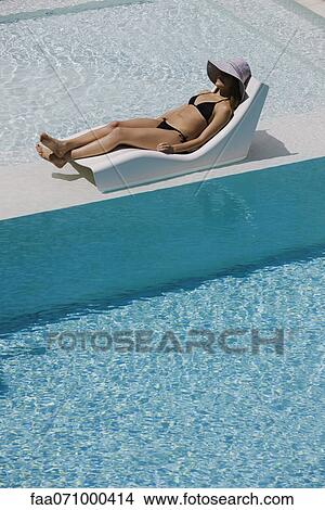 Young woman wearing sun hat reclining on poolside deckchair View Large Photo Image Picture - Young woman wearing sun hat reclining on poolside deckchair. Fotosearch