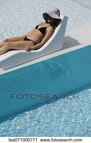 Young woman wearing sun hat reclining on poolside deckchair View Large Photo Image Stock Image - Young woman wearing sun hat reclining on poolside deckchair. Fotosearch