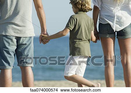 Picture - Boy holding parents' hands at the beach, rear view. Fotosearch