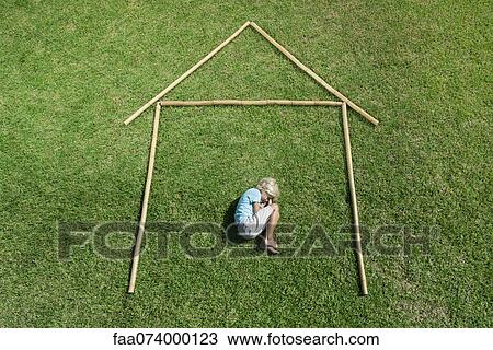 Stock Image - Boy in fetal position within outline of house, high angle view. Fotosearch