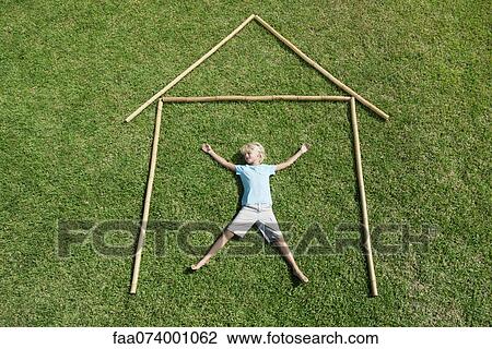 Stock Image - Boy lying on grass within outline of house, high angle view. Fotosearch