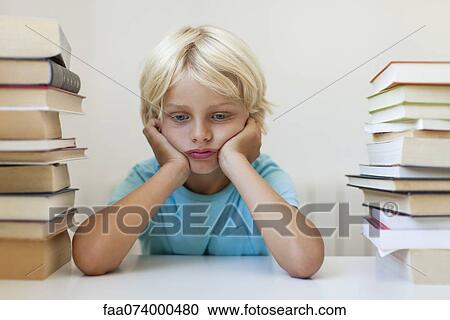 Stock Image - Boy sitting between two stacks of books, sulking. Fotosearch