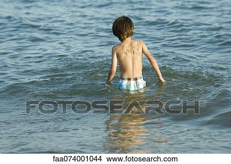 Picture - Boy wading in water, rear view. Fotosearch