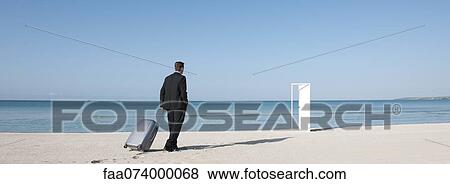 Businessman pulling suitcase on beach, walking towards half-open door View Large Photo Image Stock Photo - Businessman pulling suitcase on beach, walking towards half-open door. Fotosearch