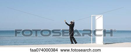 Businessman standing on beach looking at ocean with arms raised, rear view View Large Photo Image Picture - Businessman standing on beach looking at ocean with arms raised, rear view. Fotosearch