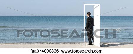 Stock Photograph - Businessman standing on beach looking at ocean, seen through open door. Fotosearch