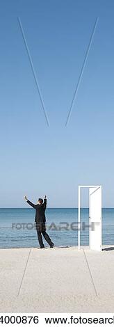 Businessman standing on beach looking at ocean with arms raised View Large Photo Image Stock Photograph - Businessman standing on beach looking at ocean with arms raised. Fotosearch