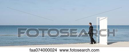 Businessman standing on beach next to half-open door, looking at ocean View Large Photo Image Picture - Businessman standing on beach next to half-open door, looking at ocean. Fotosearch