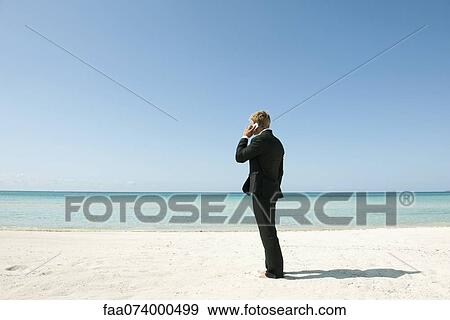 Businessman talking on cell phone while standing on beach, rear view View Large Photo Image Stock Photo - Businessman talking on cell phone while standing on beach, rear view. Fotosearch