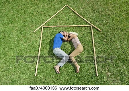 Couple lying on grass within outline of house, high angle view View Large Photo Image Stock Photograph - Couple lying on grass within outline of house, high angle view. Fotosearch