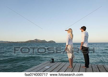 Couple standing on pier looking at view, side view View Large Photo Image Stock Photo - Couple standing on pier looking at view, side view. Fotosearch