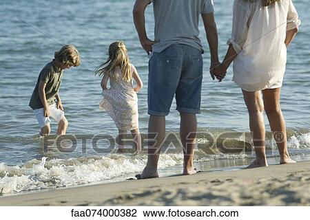 Stock Image - Family at the beach, parents watching as children play in surf. Fotosearch