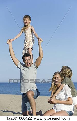 Family playing together at the beach, girl standing on her father's shoulders View Large Photo Image Stock Image - Family playing together at the beach, girl standing on her father's shoulders. Fotosearch