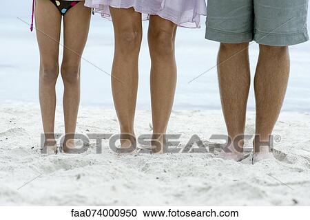 Stock Image - Family standing on beach, low section. Fotosearch