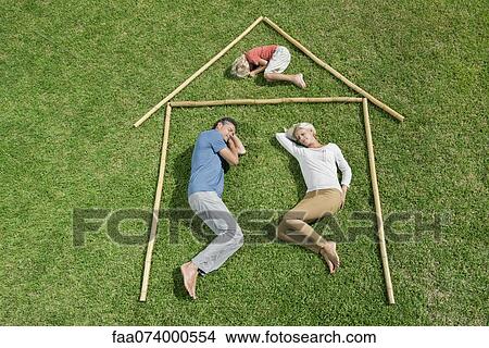 Picture - Family with one child lying on grass within outline of house, high angle view. Fotosearch