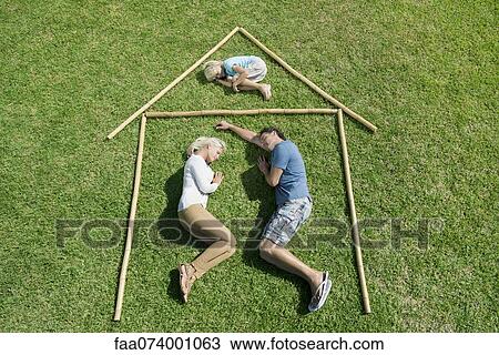 Stock Image - Family with one child lying on grass within outline of house, high angle view. Fotosearch