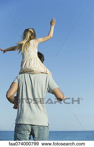 Stock Photo - Father carrying daughter on his shoulders, rear view. Fotosearch