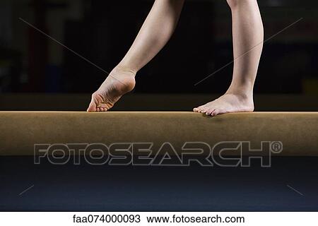 Stock Image - Female gymnast on balance beam, low section. Fotosearch
