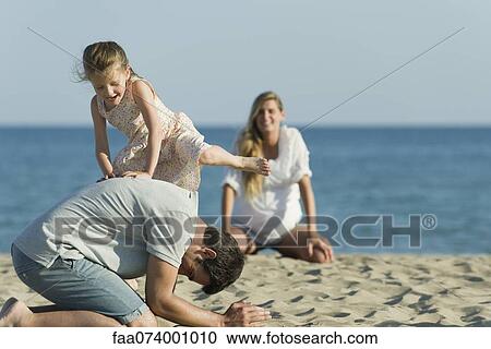 Stock Image - Girl playing with her father at the beach. Fotosearch