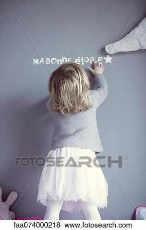 Little girl looking at words printed on wall, rear view View Large Photo Image Stock Photo - Little girl looking at words printed on wall, rear view. Fotosearch