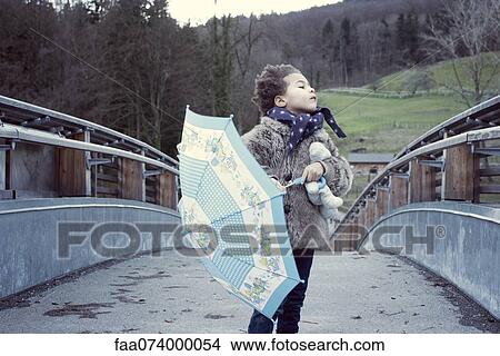 Picture - Little girl walking on bridge with umbrella, looking away. Fotosearch