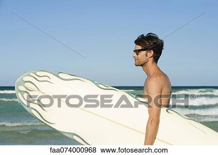 Stock Photo - Man carrying surfboard at the beach. Fotosearch