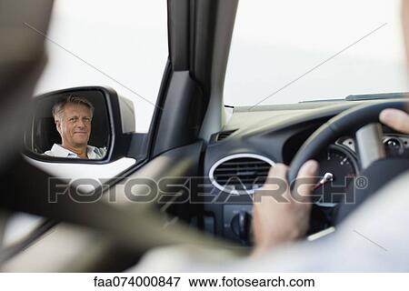 Stock Photo - Man driving car, reflected in driver's side mirror. Fotosearch