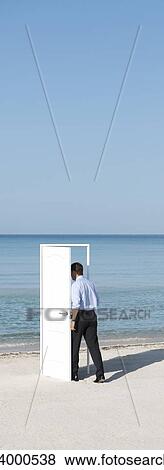 Stock Photo - Man entering open door on beach, rear view. Fotosearch