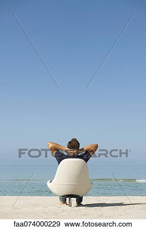 Man sitting in armchair on beach looking at ocean, rear view View Large Photo Image Stock Photo - Man sitting in armchair on beach looking at ocean, rear view. Fotosearch