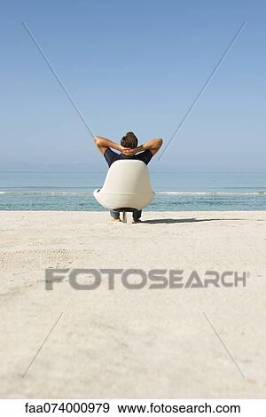 Man sitting in armchair on beach looking at ocean, rear view View Large Photo Image Stock Photo - Man sitting in armchair on beach looking at ocean, rear view. Fotosearch
