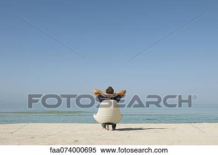 Man sitting in armchair on beach looking at ocean, rear view View Large Photo Image Stock Photography - Man sitting in armchair on beach looking at ocean, rear view. Fotosearch