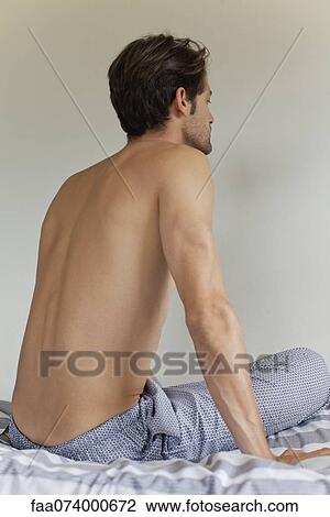 Stock Image - Man sitting on bed, rear view. Fotosearch