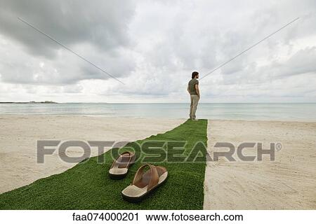Man standing at end of carpet on beach, sandals on foreground View Large Photo Image Stock Image - Man standing at end of carpet on beach, sandals on foreground. Fotosearch