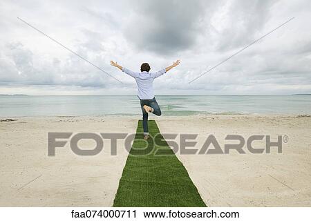 Man standing on one leg at end of carpet on beach with arms outstretched, rear view View Large Photo Image Stock Image - Man standing on one leg at end of carpet on beach with arms outstretched, rear view. Fotosearch