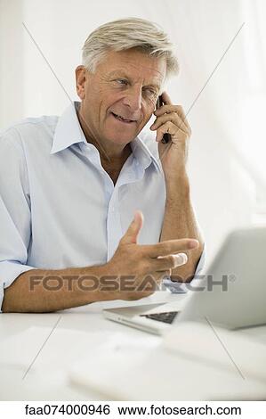 Stock Photograph - Man talking on cell phone while using laptop computer. Fotosearch