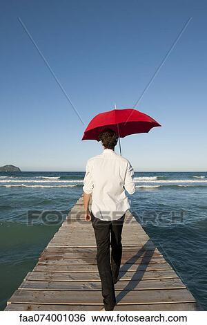 Man walking on pier with red umbrella, rear view View Large Photo Image Stock Photograph - Man walking on pier with red umbrella, rear view. Fotosearch