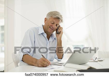 Stock Photo - Man working at home, talking on cell phone. Fotosearch