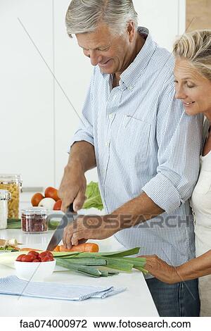 Stock Image - Mature couple preparing food together in kitchen. Fotosearch