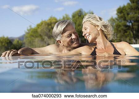 Stock Image - Mature couple relaxing together in pool. Fotosearch