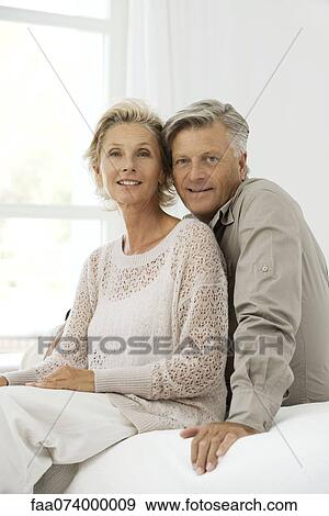 Stock Photo - Mature couple sitting together on bed, portrait. Fotosearch