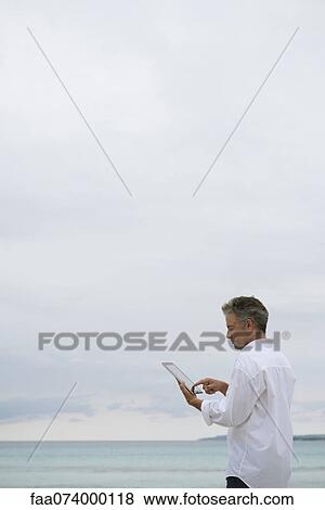 Stock Photo - Mature man using digital tablet by ocean. Fotosearch