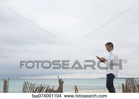Picture - Mature man using digital tablet on beach. Fotosearch