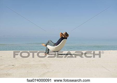 Mid-adult man relaxing in armchair on beach View Large Photo Image Stock Image - Mid-adult man relaxing in armchair on beach. Fotosearch