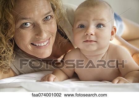 Stock Image - Mother lying down beside baby, portrait. Fotosearch