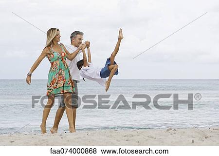 Stock Photo - Parents swinging daughter while walking on beach. Fotosearch
